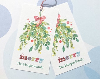 May include: Two rectangular gift tags with a watercolor design of mistletoe and a red bow. The word "merry" is printed in colorful letters, and the text "The Morgan Family" is below. A red and white string is attached.