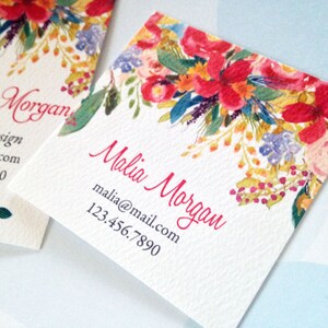 K&ouml;nnte beinhalten: Zwei quadratische Visitenkarten mit einem Aquarell-Blumenmuster. Die Karten zeigen rote, rosa, gelbe und blaue Blumen. Der Name "Malia Morgan" steht in roter Schrift, zusammen mit den Kontaktdaten.