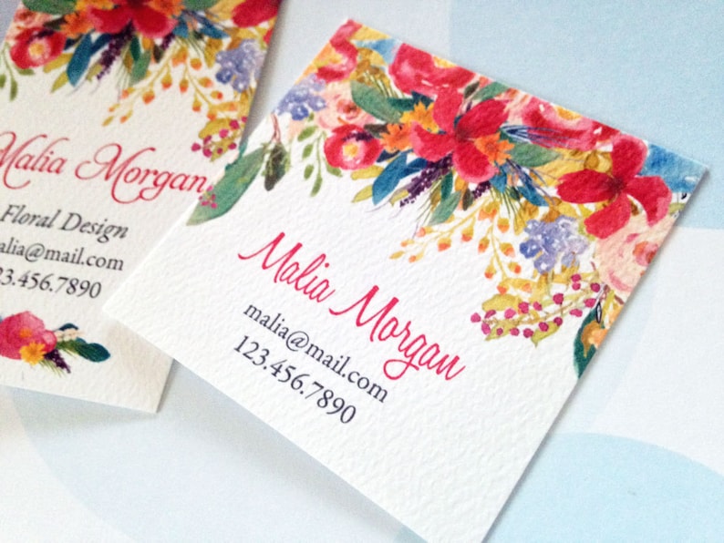 K&ouml;nnte beinhalten: Zwei quadratische Visitenkarten mit einem Aquarell-Blumenmuster. Die Karten zeigen rote, rosa, gelbe und blaue Blumen. Der Name "Malia Morgan" steht in roter Schrift, zusammen mit den Kontaktdaten.