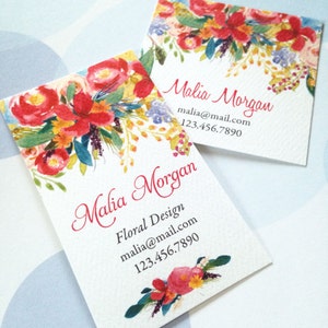 K&ouml;nnte beinhalten: Zwei quadratische Visitenkarten mit einem Aquarell-Blumenmuster. Die Karten zeigen eine lebendige Anordnung von roten, orangen und gelben Blumen mit gr&uuml;nen und blauen Akzenten. Der Name "Malia Morgan" ist in Schreibschrift geschrieben, zusammen mit Kontaktinformationen.