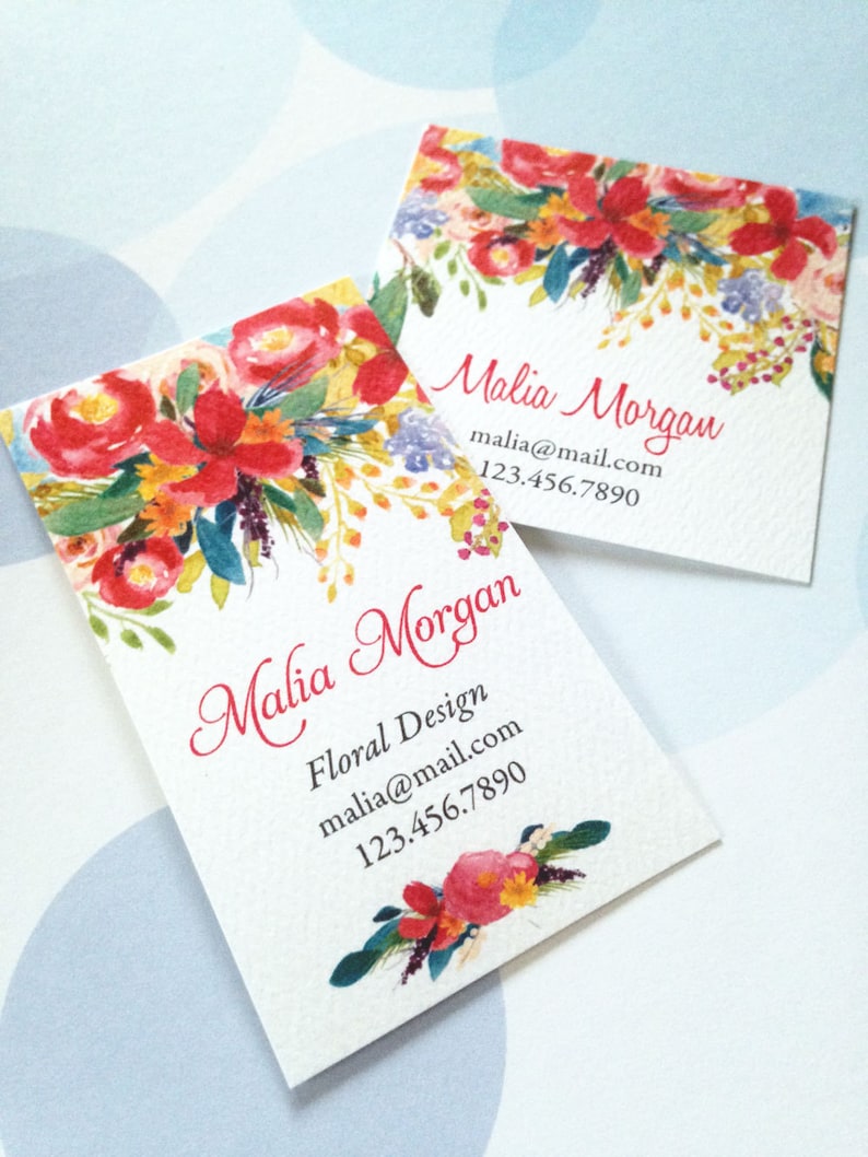 K&ouml;nnte beinhalten: Zwei quadratische Visitenkarten mit einem Aquarell-Blumenmuster. Die Karten zeigen eine lebendige Anordnung von roten, orangen und gelben Blumen mit gr&uuml;nen und blauen Akzenten. Der Name "Malia Morgan" ist in Schreibschrift geschrieben, zusammen mit Kontaktinformationen.