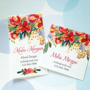 K&ouml;nnte beinhalten: Zwei Visitenkarten mit floralem Design. Die Karten zeigen ein Aquarelldesign aus roten, orangefarbenen und gelben Blumen mit gr&uuml;nen Bl&auml;ttern. Der Text "Malia Morgan" ist in Schreibschrift gehalten, mit Kontaktinformationen darunter.
