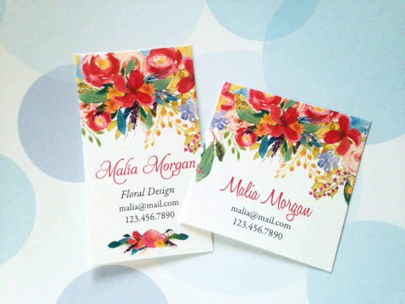 K&ouml;nnte beinhalten: Zwei Visitenkarten mit floralem Design. Die Karten zeigen ein Aquarelldesign aus roten, orangefarbenen und gelben Blumen mit gr&uuml;nen Bl&auml;ttern. Der Text "Malia Morgan" ist in Schreibschrift gehalten, mit Kontaktinformationen darunter.