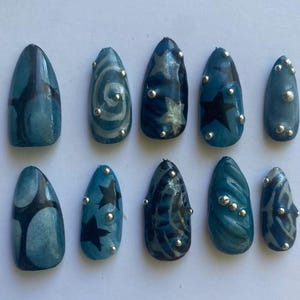 May include: Ten blue and silver press-on nails with different designs, including stars, swirls, and abstract patterns.