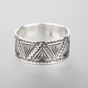 May include: A silver ring with a geometric pattern of triangles. The ring is wide and has a polished finish.