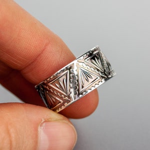 May include: A silver ring with a geometric pattern. The ring is wide and has a triangular design.