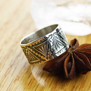 May include: A silver ring with a geometric design. The ring is made of sterling silver and has a wide band. The design features a series of triangles and lines.