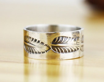 Puede incluir: Un anillo de banda de plata con un diseño de hojas. El anillo es ancho y tiene un acabado liso y pulido.