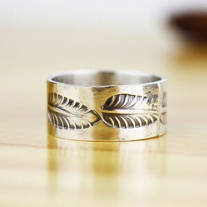 May include: A silver band ring with a leaf design. The ring is wide and has a smooth, polished finish.