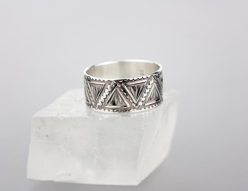 May include: A silver band ring with a geometric pattern of triangles. The ring is wide and has a polished finish.