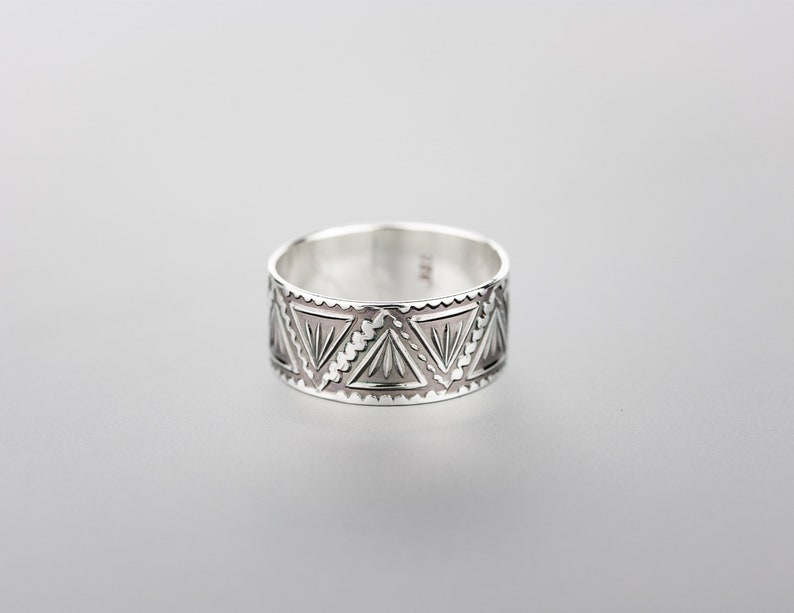 May include: A silver ring with a geometric pattern of triangles. The ring is wide and has a polished finish.