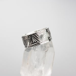 May include: A silver ring with a geometric design. The ring is on a clear crystal stand.