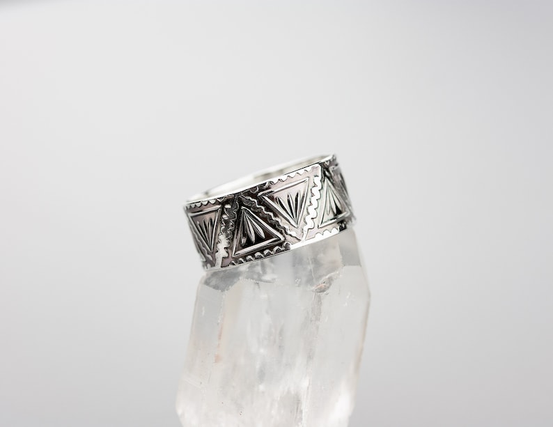 May include: A silver ring with a geometric design. The ring is on a clear crystal stand.