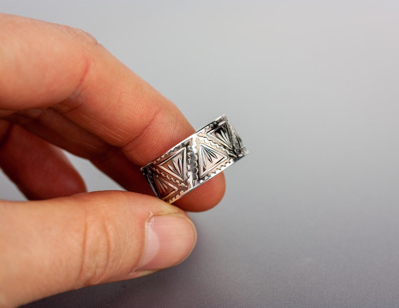 May include: A silver ring with a geometric pattern. The ring is wide and has a triangular design.