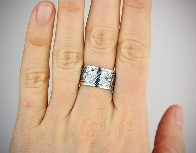 May include: A silver ring with a geometric pattern. The ring is worn on a finger.
