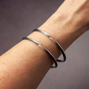 May include: Two silver bangle bracelets stacked on a person's wrist.