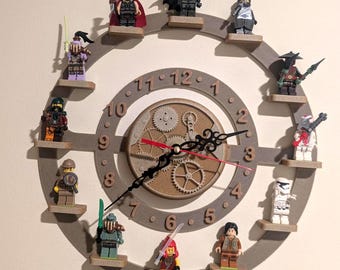 May include: A circular wall clock featuring a tan frame with twelve small wooden platforms, each holding a unique plastic minifigure. The clock face displays numbers one through twelve, with a central gear mechanism and black hour and minute hands.