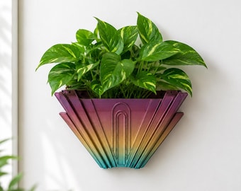 May include: A wall-mounted planter with a geometric fan-shaped design featuring a gradient color transition from deep purple at the top to gold in the center and teal at the bottom, containing a lush green pothos plant with variegated leaves.