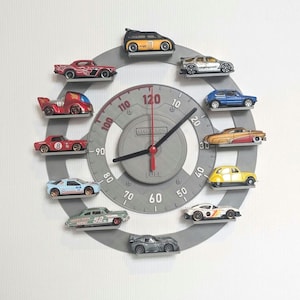 Könnte beinhalten: Eine graue Wanduhr mit Tachometer-Design, mit Miniatur-Spielzeugautos als Stundenmarkierungen. Die Zeiger der Uhr sind schwarz und rot. Das Wort "FUEL" ist auf dem Zifferblatt aufgedruckt.