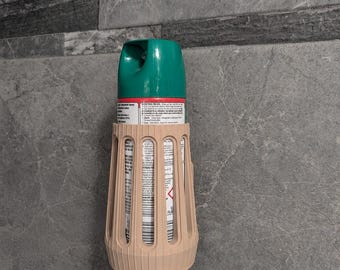 May include: A beige plastic holder with vertical slats mounted on a wall, containing a cylindrical aerosol spray can. The can features a green plastic nozzle cap and a white label with printed text and warning symbols visible through the slats.