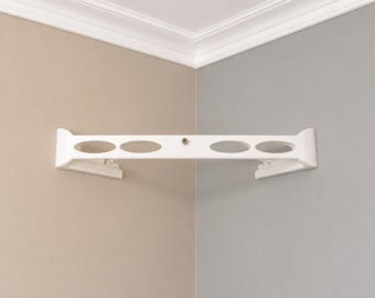 May include: A white corner shelf featuring a horizontal frame with four oval-shaped cutouts and a single metal screw centered on the front edge. The shelf is mounted flush against two perpendicular walls, providing a stable structure for storage.