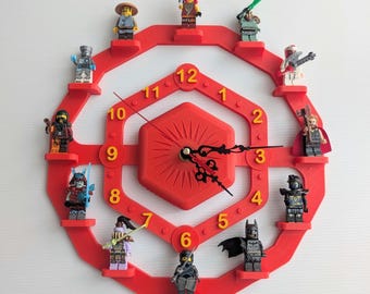 May include: A red wall clock with a hexagonal center and a circular outer frame featuring twelve small platforms. Each platform holds a unique plastic minifigure character. The clock face displays yellow numbers from one to twelve.