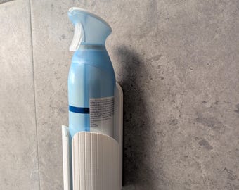 May include: A white, vertically ribbed plastic wall-mounted holder securely cradling a light blue aerosol spray bottle. The holder features a semi-circular design with a vertical cutout, providing a stable storage solution for the spray container.