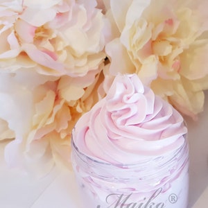May include: A close-up of a jar of pink whipped body butter with the word "Maiko" in cursive script on the jar. The jar is surrounded by white and pink peonies.