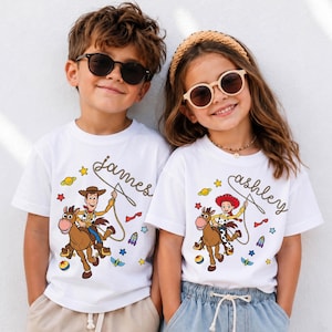 May include: Two white short-sleeved t-shirts featuring Toy Story character graphics. One shirt displays Woody riding Bullseye with the name James, and the other shows Jessie riding Bullseye with the name Ashley, both surrounded by colorful space icons.