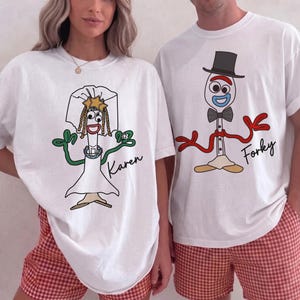 May include: Two white crewneck t-shirts featuring cartoon character graphics. The left shirt displays a character in a wedding veil and dress with the name Karen. The right shirt shows a character in a top hat and bowtie with the name Forky.