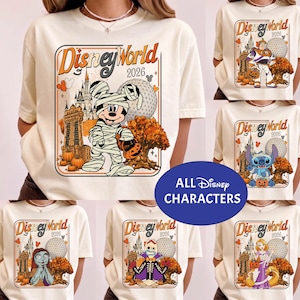 May include: A cream-coloured short-sleeve t-shirt featuring a graphic print of Disney World 2026 with various characters in Halloween costumes, including Mickey Mouse as a mummy, Buzz Lightyear, Stitch, Sally, Forky, and Rapunzel with pumpkins.