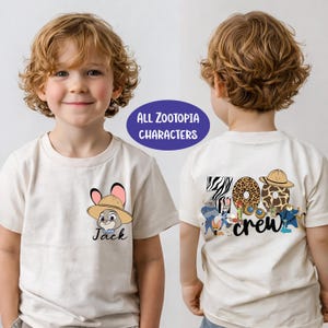 May include: A cream-colored short-sleeve t-shirt featuring a graphic of a rabbit character wearing a safari hat on the front left chest with the name Jack. The back displays the text Zoo crew with various Zootopia character illustrations.