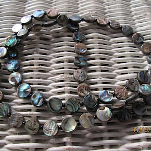May include: A double strand necklace made of iridescent abalone shell beads with black spacers. The necklace is on a woven wicker surface.