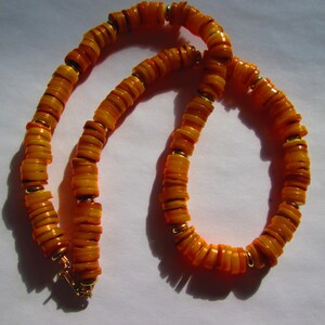 May include: A necklace composed of flat, round, orange and yellow beads. The beads are strung together with small gold-colored spacers. The necklace has a gold-colored clasp.
