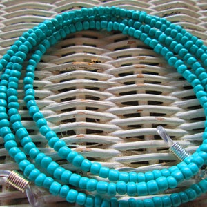 May include: Turquoise blue beaded eyeglass chain with silver metal clasps. The chain is made of small, round beads and is designed to hold eyeglasses around the neck.