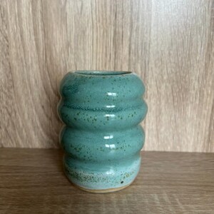 Könnte beinhalten: Eine tealfarbene Keramikvase mit einem strukturierten, wellenförmigen Design. Die Vase hat eine hellblaue und weiße Glasur.