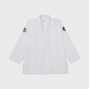 May include: A white martial arts uniform, or gi, with a V-neck design. The gi has black circular patches on the shoulders and a pink tag at the neck. The sleeves are long and the gi is made of a sturdy fabric.