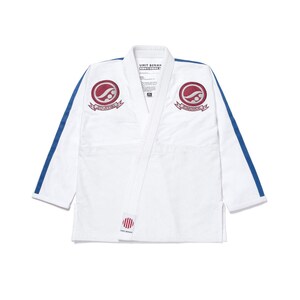 Peut inclure: Uniforme d'arts martiaux blanc avec des rayures bleues sur les manches et un emblème bordeaux sur la poitrine. Le texte "UMIT BENAN" et "KNOTHOLE" est visible sur le col.