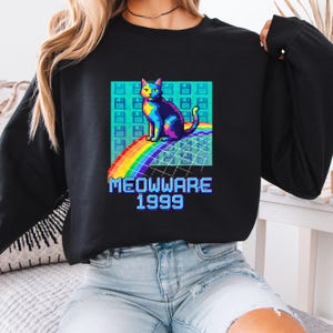 May include: Black sweatshirt featuring a pixelated cat design in vibrant rainbow colors, sitting on a rainbow. The graphic includes the text "MEOWWARE 1999" in a retro font, set against a background of floppy disk icons.
