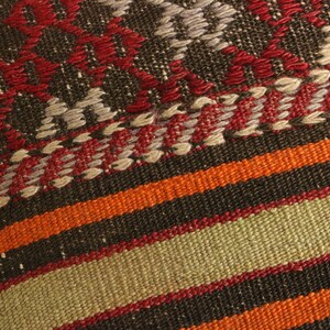 May include: Close-up of a woven fabric with a geometric pattern in shades of red, orange, brown, and beige.