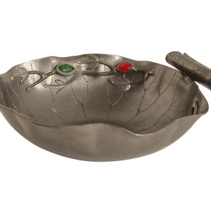Puede incluir: Un cuenco de plata con un diseño de hoja y detalles en verde y rojo. El cuenco tiene un asa con forma de hoja.