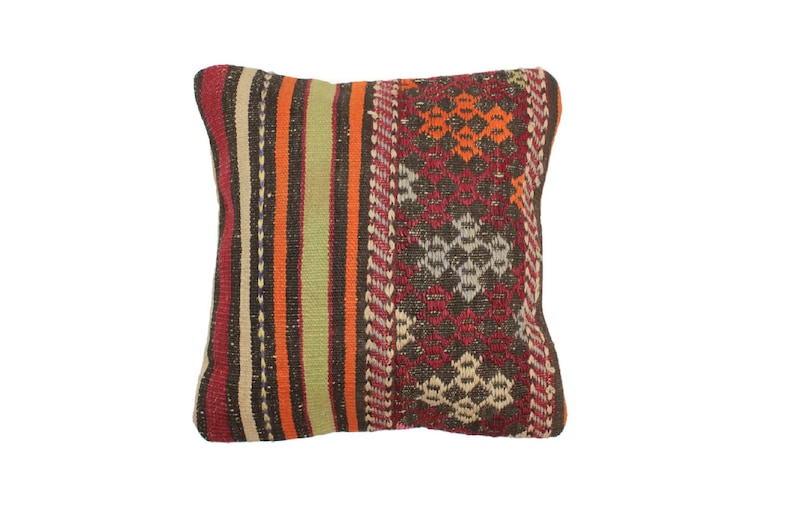 May include: A colorful throw pillow with a geometric pattern in shades of red, orange, brown, and green. The pillow is made of woven fabric and has a fringed edge.