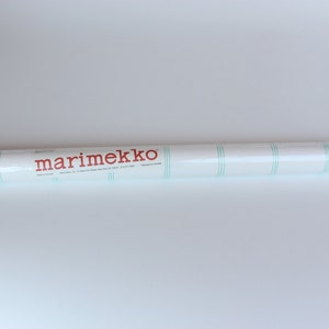 May include: A white roll of marimekko wallpaper with green stripes. The roll is labeled "marimekko" in red.
