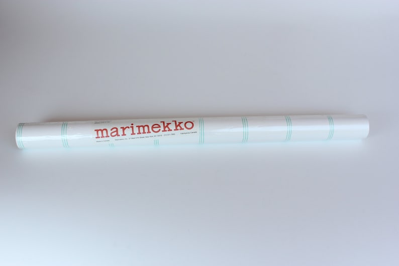 May include: A white roll of marimekko wallpaper with green stripes. The roll is labeled "marimekko" in red.
