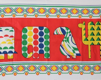 May include: White fabric with a red stripe featuring four colorful animal silhouettes: an elephant with green and yellow semi-circles, an elephant with red, blue, and green circles, a bird with green, yellow, and blue stripes, and a camel with green triangles. The fabric has a green, white, and yellow border.