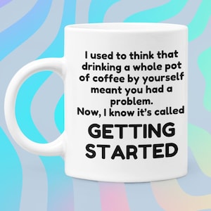 May include: White ceramic coffee mug with black text that reads: "I used to think that drinking a whole pot of coffee by yourself meant you had a problem. Now, I know it's called GETTING STARTED."