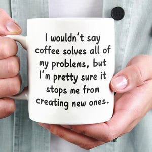 May include: White ceramic coffee mug with black text that reads "I wouldn't say coffee solves all of my problems, but I'm pretty sure it stops me from creating new ones."