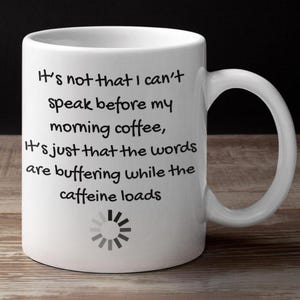 May include: White ceramic coffee mug with a black handle. The mug features the text: "It's not that I can't speak before my morning coffee, It's just that the words are buffering while the caffeine loads."