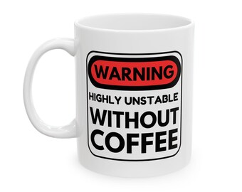Op de afbeelding: Witte keramische koffiemok met een zwart en rood waarschuwingslabel met de tekst "WARNING HIGHLY UNSTABLE WITHOUT COFFEE". De mok heeft een gebogen handvat en is ontworpen voor warme dranken.