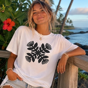 May include: A white short-sleeved t-shirt featuring a black graphic print of four stylized flowers arranged in a symmetrical cross pattern on the chest. The shirt has a crew neckline and a relaxed fit, made of a plain white fabric.